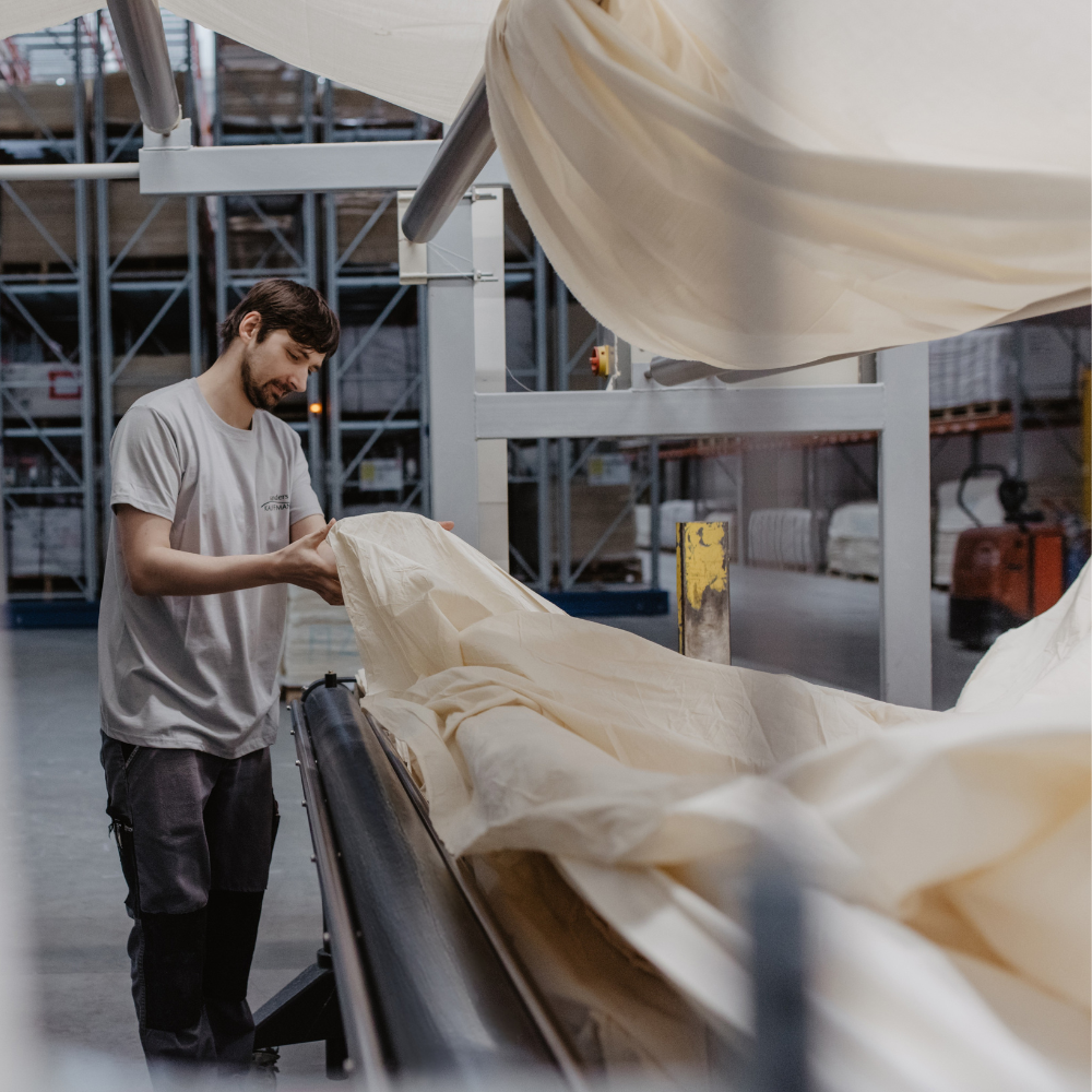 Ein Mitarbeiter steht an einer Maschine und kontrolliert das Rohgewebe.